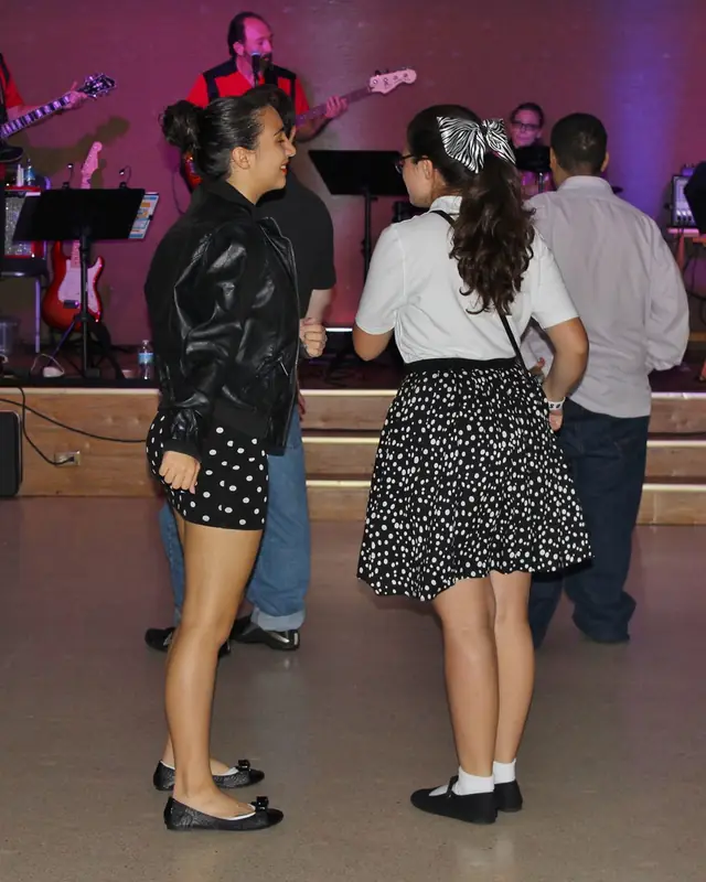 Two volunteers in 1950s outfits dancing toward the band